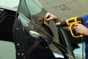 Worker tinting car window with heat gun in workshop, closeup